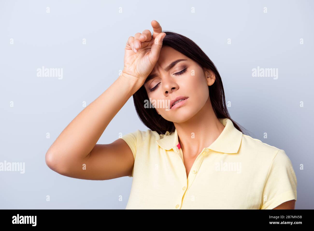 Young hispanic lady in a casual clothes on light blue background is holding her hand near the forehead. She is tired and don`t feel well Stock Photo